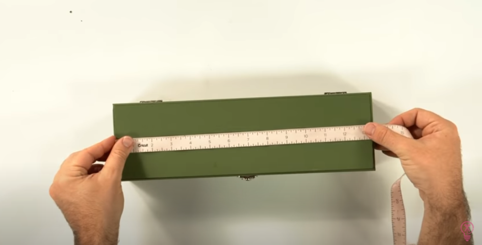 Using A Measuring Tape To Measure The Top Of A Green Box